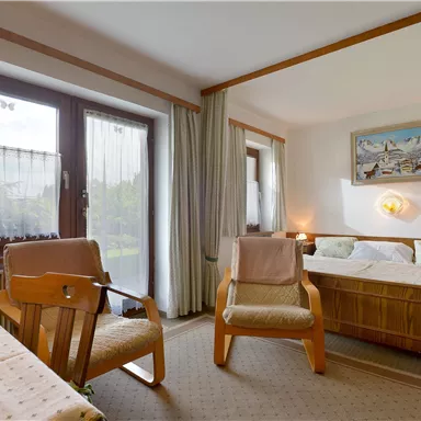 A cozy bedroom with a double bed and a table.  
Large windows let in plenty of light and offer a beautiful view outside.