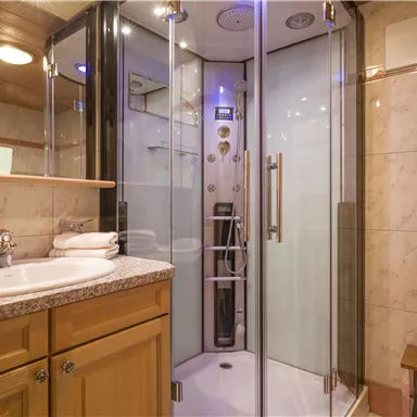 Ein modernes Badezimmer mit einer Glasdusche und einer hellen Holzverkleidung. Der Waschtisch ist aus Granit und bietet frische Handtücher.