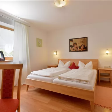 A bright bedroom with two beds and a large window. The room is nicely furnished and has wooden floors.