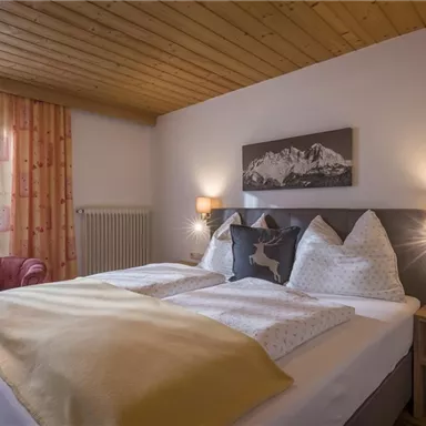 Ein gemütliches Schlafzimmer mit einem großen Bett und Holzdecke. Die Atmosphäre ist einladend, mit einem roten Sessel und viel natürlichem Licht.