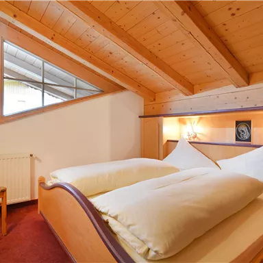Ein gemütliches Schlafzimmer mit zwei Einzelbetten und Holzverkleidung. Ein Stuhl steht neben dem Bett, und ein Fenster lässt viel Tageslicht herein.