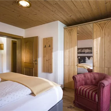 Ein gemütliches Schlafzimmer mit einem großen Bett und einer roten Sessel. Der Raum hat Holzdecken und stilvolle Möbel.