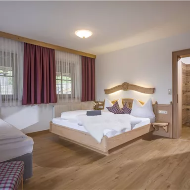 A cozy bedroom with two beds. The decor is modern, featuring wood and soft colors, as well as large windows that let in plenty of light.