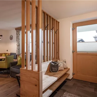 An inviting entrance area with wood paneling and a cozy seating area. In the background, there is a modern dining area with colorful chairs and a large window front.