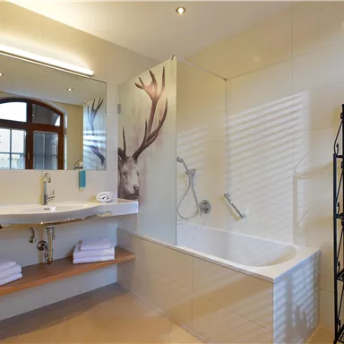 A modern bathroom with a bathtub and a large mirror. Clean towels are neatly placed on a shelf.