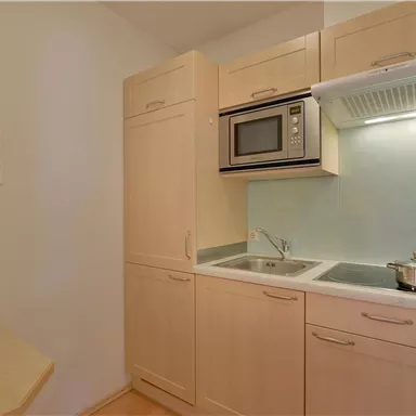 Eine moderne Küche mit hellen Holzschränken und einer Mikrowelle. Es gibt einen kleinen Herd und eine Spüle, ideal für die Zubereitung von Mahlzeiten.