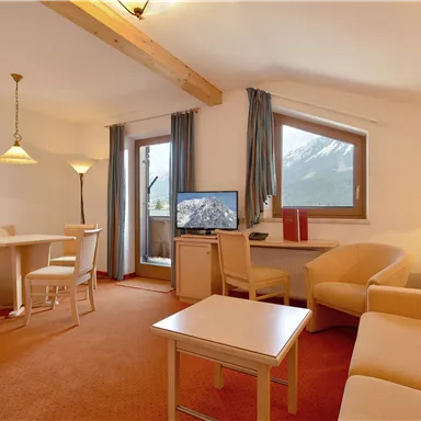 Ein gemütliches Wohn- und Esszimmer mit einem Tisch, Stühlen und einem Fernseher. Große Fenster bieten einen Blick auf die Berge.