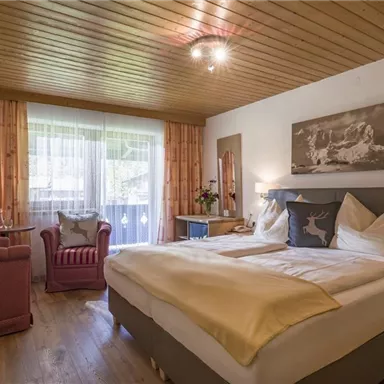 Ein gemütliches Schlafzimmer mit Holzdecke und einem großen Bett. Das Zimmer verfügt über ein rotes Sessel, einen Fernseher und viel Tageslicht.