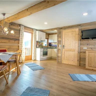 A cozy living space with wooden walls and modern furniture. The kitchen is well-equipped, and there is a dining area with wooden chairs.