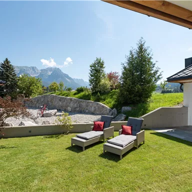 Ein schöner Garten mit Liegestühlen und Blick auf Berge. Der Himmel ist klar und sonnig.
