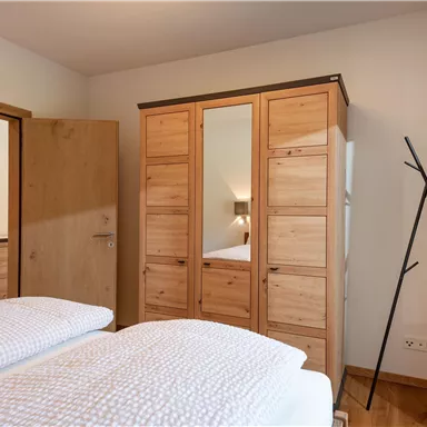 Ein gemütliches Schlafzimmer mit zwei Einzelbetten und einem Holzschrank. Die Wände sind hell und es gibt einen modernen Kleiderständer.