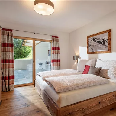 Ein gemütliches Schlafzimmer mit einem Doppelbett und Holzmöbel. Große Fenster sorgen für viel Licht und einen Blick auf die Natur.