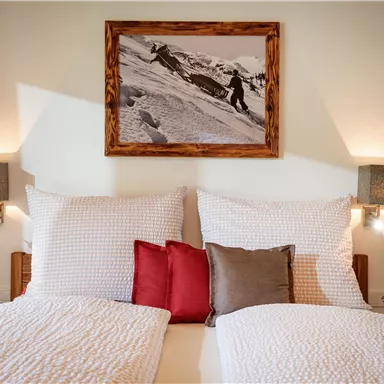 Ein einladendes Schlafzimmer mit zwei Betten und gemütlichen Kissen. An der Wand hängt ein schönes Bild einer Schneelandschaft.