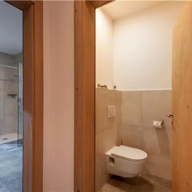 Ein modernes Badezimmer mit einer Dusche und einem WC. Helle Fliesen und Holzverkleidungen schaffen eine angenehme Atmosphäre.