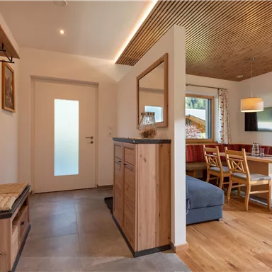 Ein gemütlicher Eingangsbereich mit Holzregalen und einer Sitzbank. Der Raum führt zu einem Essbereich mit einem Tisch und Stühlen.