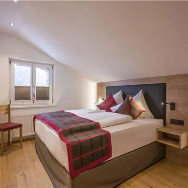 A cozy bedroom with a large double bed and wooden flooring. The room is bright and modernly furnished.