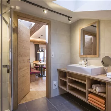 A modern bathroom with a shower and a large sink. Towels in warm colors are neatly stacked.
