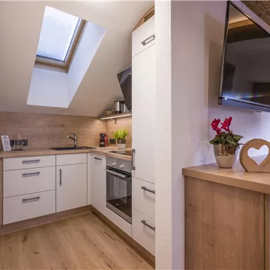 A modern kitchen with sloped roof windows and wooden surfaces. There are modern appliances and a cozy atmosphere.