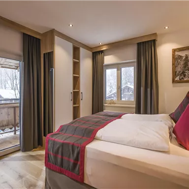 A cozy bedroom with a large bed and red pillows. The room has large windows overlooking a snowy landscape.