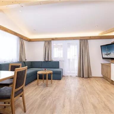 Ein modernes Wohnzimmer mit einem gemütlichen Sofa und einem Holztisch. Große Fenster sorgen für viel Tageslicht und eine einladende Atmosphäre.