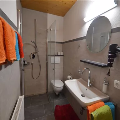A modern bathroom with a shower and a sink. Colorful towels hang on the wall.