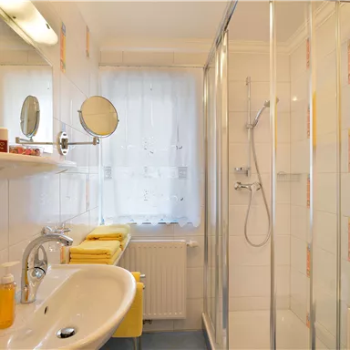 Ein modernes Badezimmer mit einer Dusche und großen Spiegeln. Gelbe Handtücher und Pflegeprodukte sind auf den Regalen platziert.