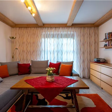 Ein modernes Wohnzimmer mit einer gemütlichen Couch und bunten Kissen. Es gibt einen Holztisch und einen Fernseher an der Wand.