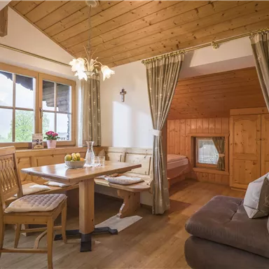 Ein gemütlicher Essbereich mit Holztisch und Stühlen, umgeben von großen Fenstern. Der Raum hat eine warme Atmosphäre mit Holzverkleidung und einem Sofa.