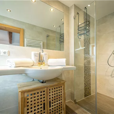 A modern bathroom with a shower and a sink. Towels and bright tiles can be seen.