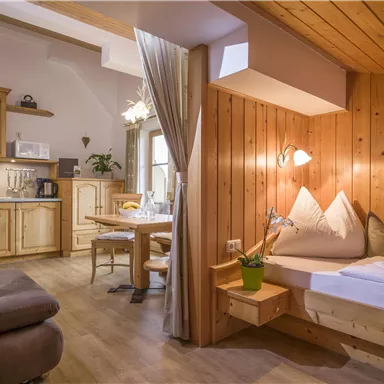 Ein gemütlicher Wohnraum mit Holzwänden und einer kleinen Küchenecke. Das Zimmer ist hell und einladend, mit einem Schlafbereich und einem Esstisch.
