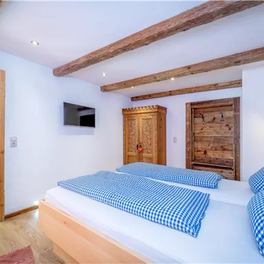 A cozy bedroom with two beds and blue pillows. Wooden beams on the ceiling and rustic furniture create an inviting atmosphere.