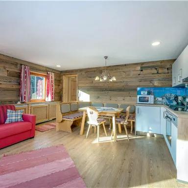 A cozy living space with a red sofa, a dining table, and a modern kitchen. The walls are clad in wood, and there are two windows that let in plenty of light.