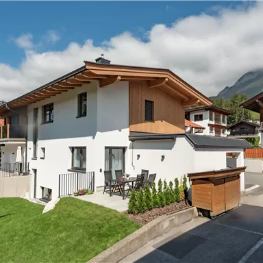 Ein modernes Haus mit einer schönen Gartenlandschaft. Im Hintergrund sind Berge und ein klarer Himmel sichtbar.