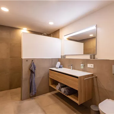 Ein modernes Badezimmer mit einer Holzwaschschublade und einem großen Spiegel. Die Wände sind in neutralen Tönen gehalten und es gibt einen Handtuchhalter.