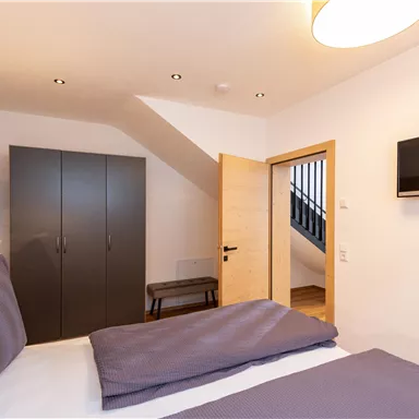 Ein modernes Schlafzimmer mit einem großen Bett und einem Fernseher an der Wand. Es gibt einen Kleiderschrank und eine gemütliche Atmosphäre.