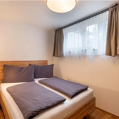 Ein gemütliches Schlafzimmer mit einem Holzbett und zwei Kissen. Weiche Vorhänge lassen das Licht sanft einfallen.