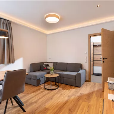 Ein modernes Wohnzimmer mit einem grauen Sofa und einem runden Tisch. Die Holzfußböden und sanfte Beleuchtung sorgen für eine einladende Atmosphäre.