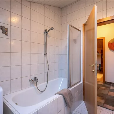 A bathroom with a bathtub and a shower. The door is open and leads to an adjacent room.