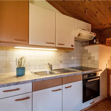 A modern kitchen with a wooden ceiling and bright cabinets. There is a sink, a stove, and various kitchen appliances.