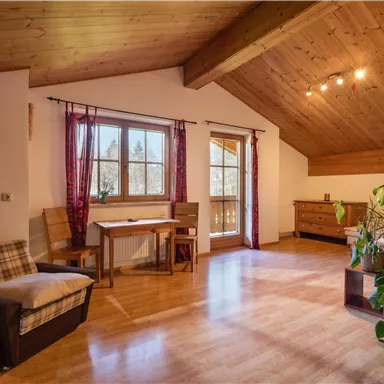 A bright room with a wooden ceiling and large windows. There is a table, chairs, and some plants in the room.