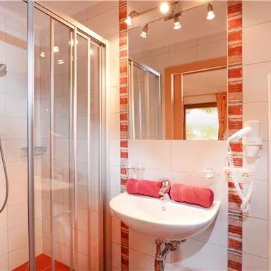 A modern bathroom with a shower and a sink. Towels in red and white stripes are neatly hung up.