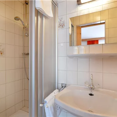 Ein modernes Badezimmer mit einer Dusche und einem Waschbecken. Die Wände sind hell gefliest und es gibt einen großen Spiegel über dem Waschbecken.