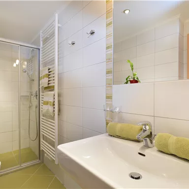 A modern bathroom with a shower and sink. A green towel and plants create a fresh atmosphere.