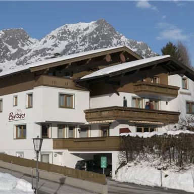 Ein gemütliches Gebäude im Alpenstil, umgeben von schneebedeckten Bergen. Der Himmel ist klar, und es liegt Schnee auf dem Boden.