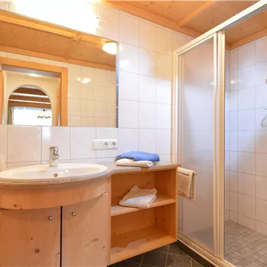 A modern bathroom with wooden shelves and a shower. The walls are brightly tiled and there is a round sink.