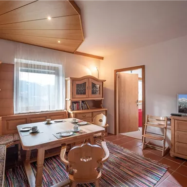 A cozy living space with wooden paneling and a large table. There is also a seating area and a television that shows a beautiful landscape.