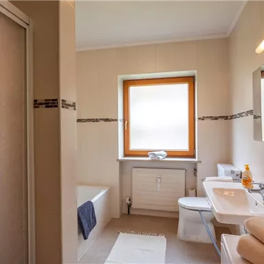 A modern bathroom with a shower, a bathtub, and a window. Towels and toiletries are placed on the sink.