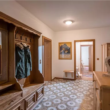 A bright hallway with wooden paneling and a coat rack. The floor has an appealing pattern, and there are accesses to several rooms.