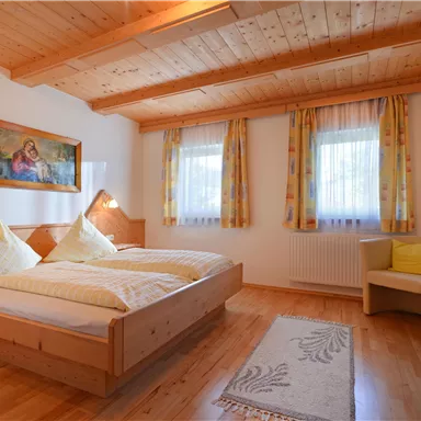 A cozy bedroom with two beds and a wooden ceiling. Bright curtains and a small table create an inviting atmosphere.