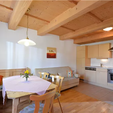 A bright and modern kitchen with a wooden beam ceiling. There is a dining area with a table and a cozy seating area.